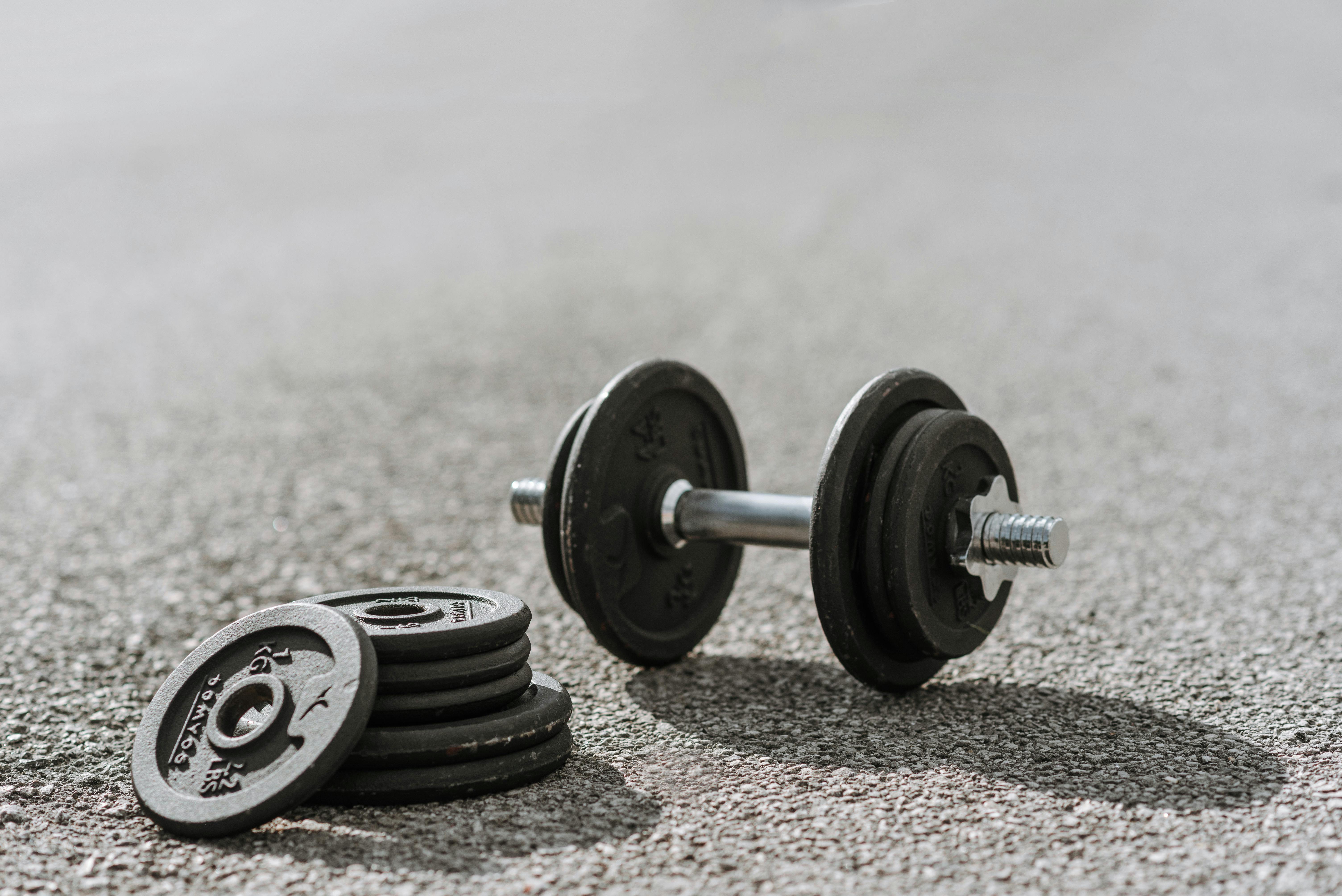Dumbbell near pile of plates on pavement in sunlight